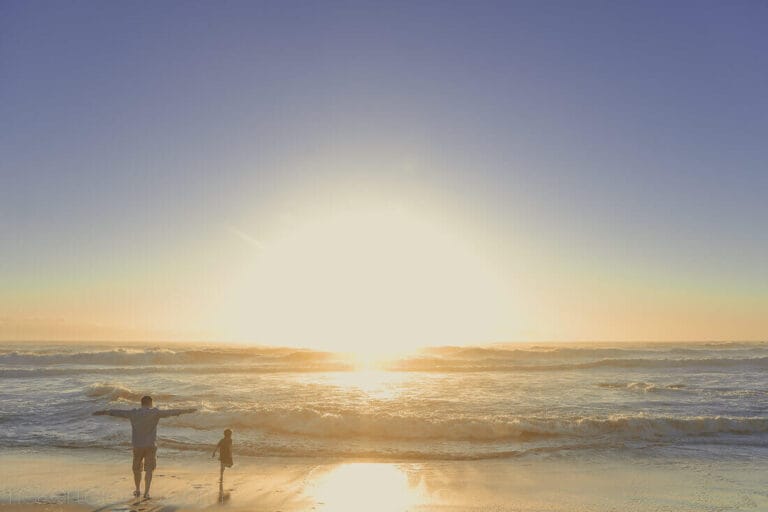 Dad and Boy standing on the beach during a sunset