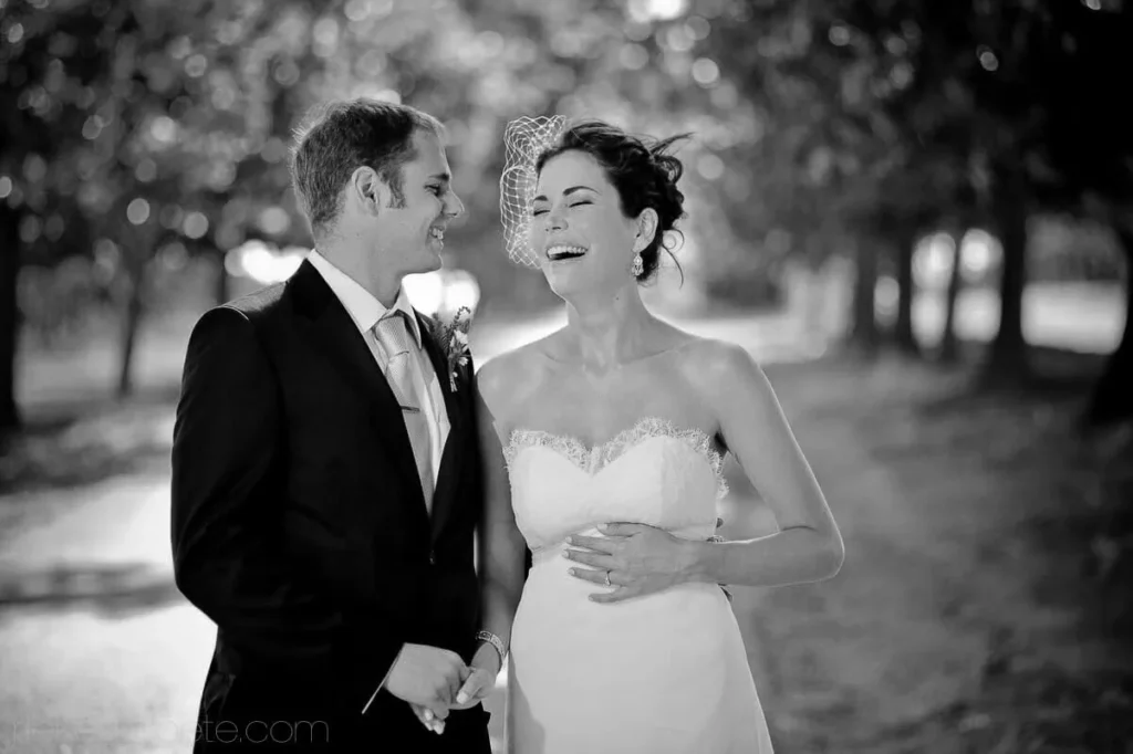 bride birdcage veil laughing groom dark suit trees