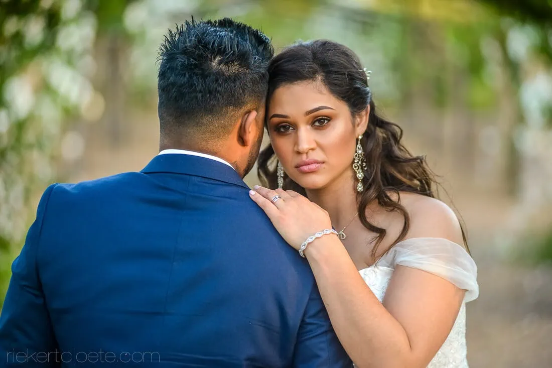 bride gazes over grooms shoulder green garden bokeh