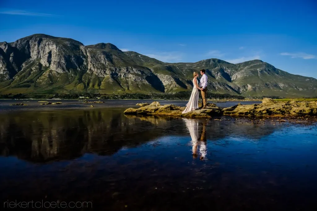 bride groom standing rocks coastal mountain reflection