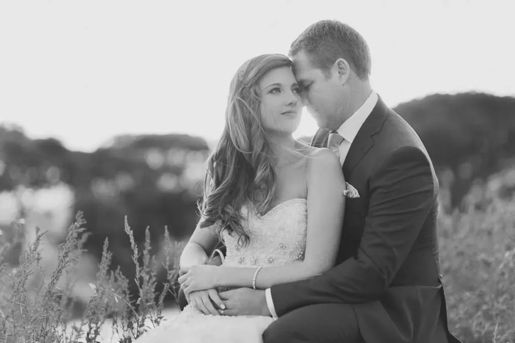 bride resting groom shoulder wild grass field bw
