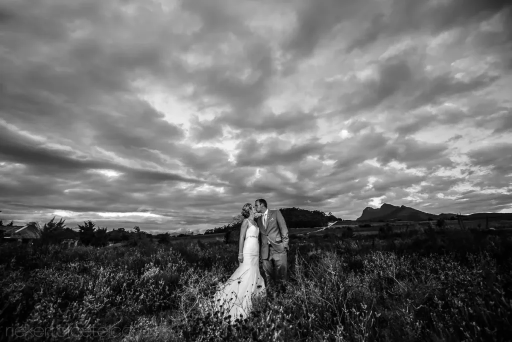 couple kissing field dramatic clouds black white