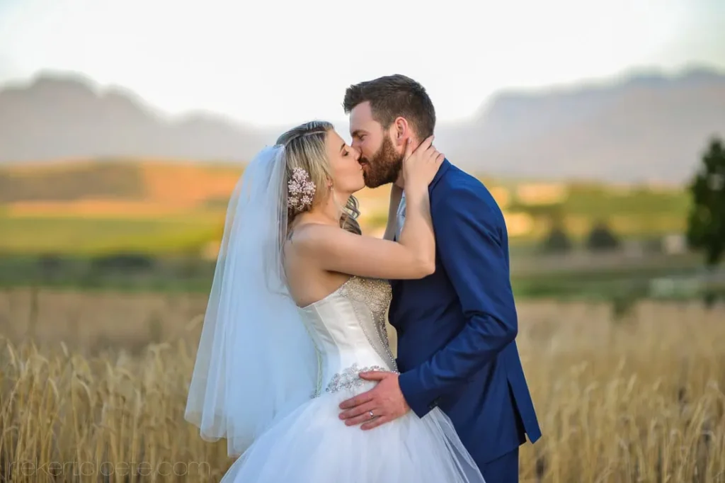 couple kissing golden wheat field mountain backdrop