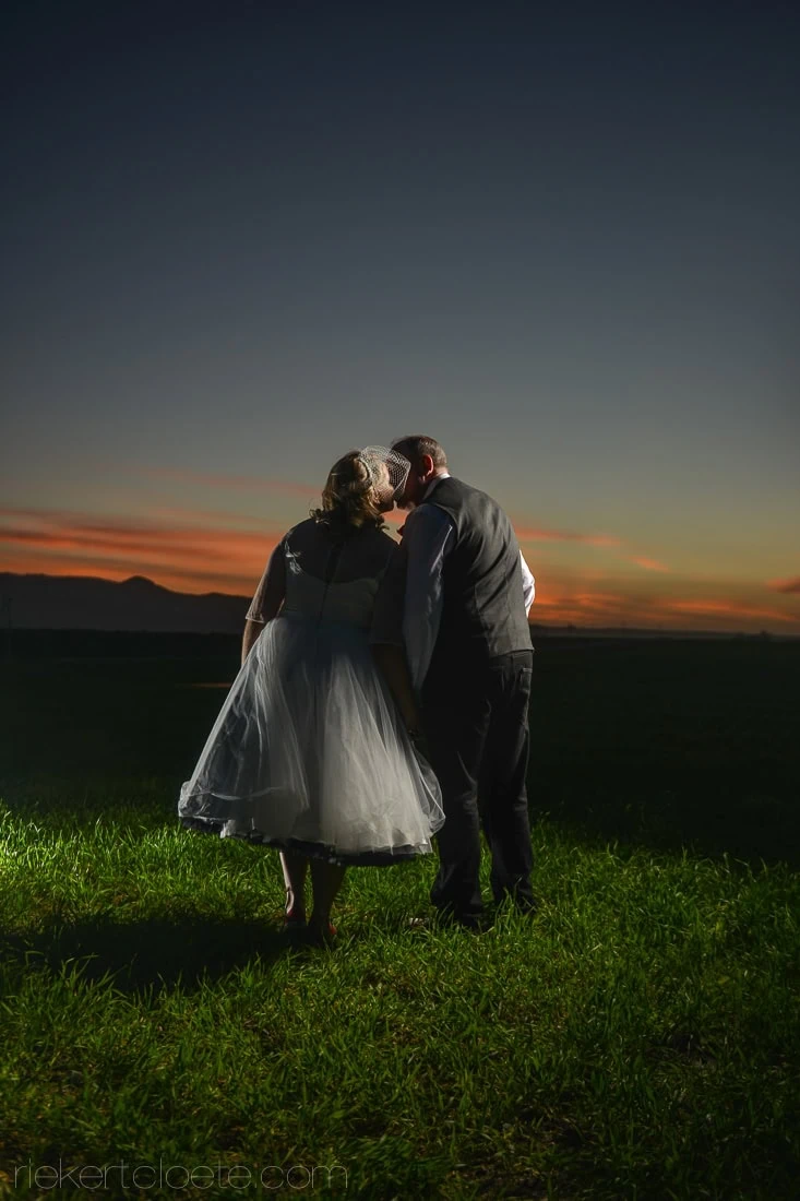 couple kissing green hillside dusk rear view
