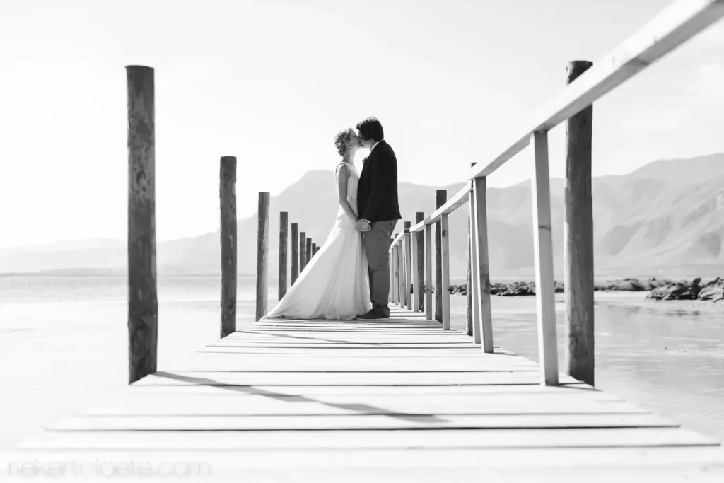 couple kissing wooden jetty mountain backdrop bw