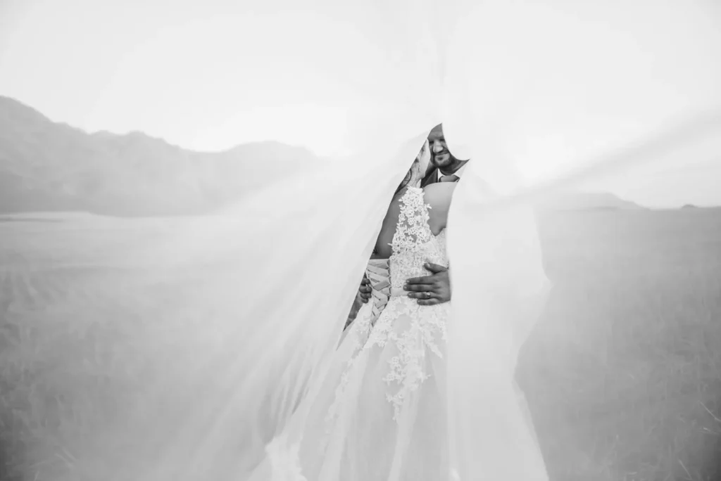 couple peek through flowing veil wheat field mountains