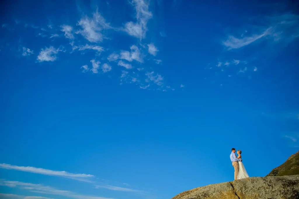 couple rocky clifftop vast blue sky wispy clouds