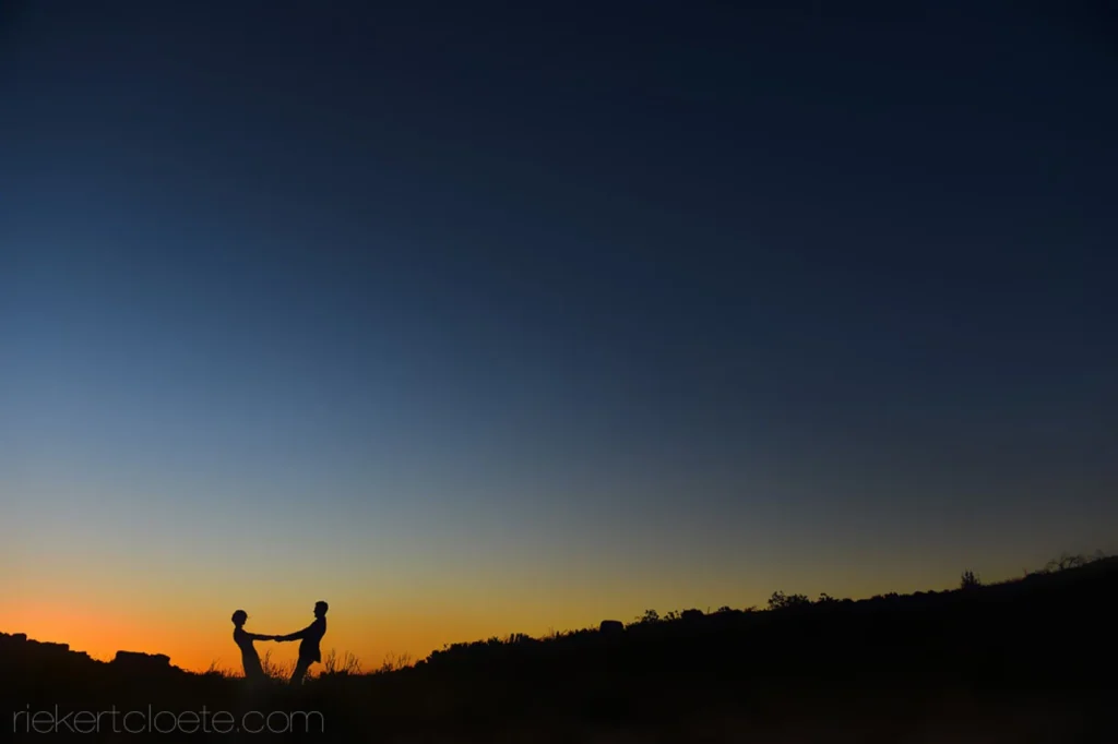 couple silhouette holding hands sunset open field