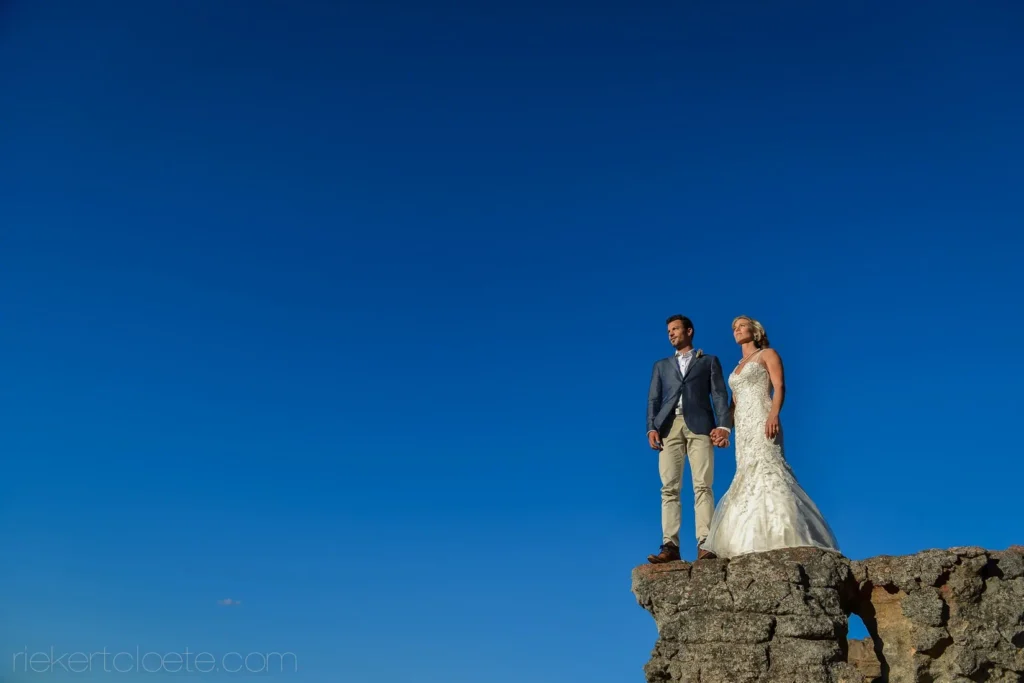 couple standing rocky cliff edge deep blue sky