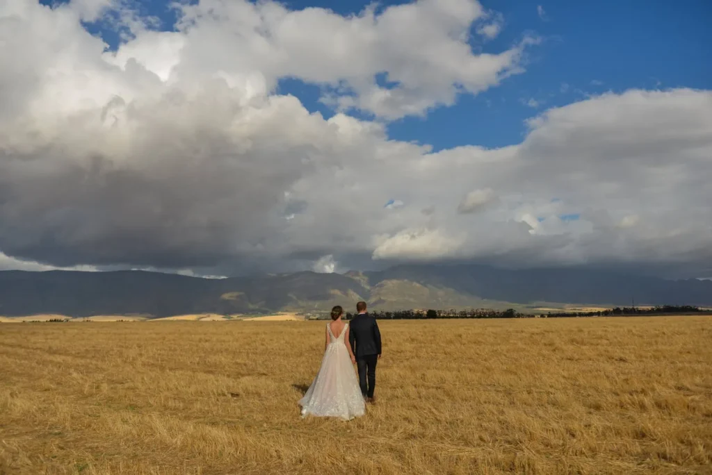 couple walking golden wheat field stormy mountain sky