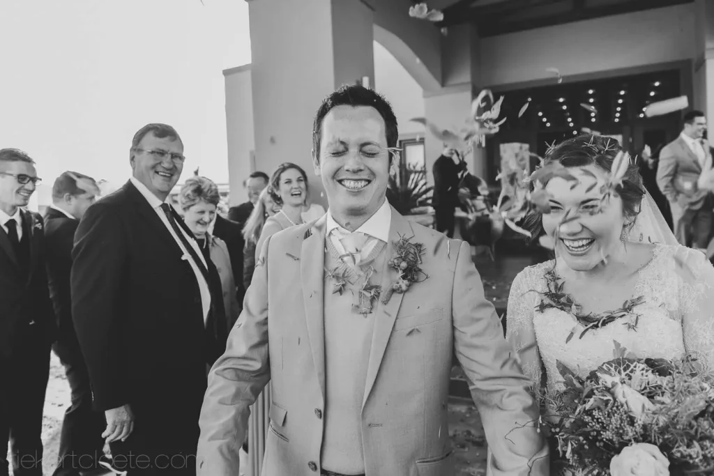 groom beige suit laughing bride confetti exit