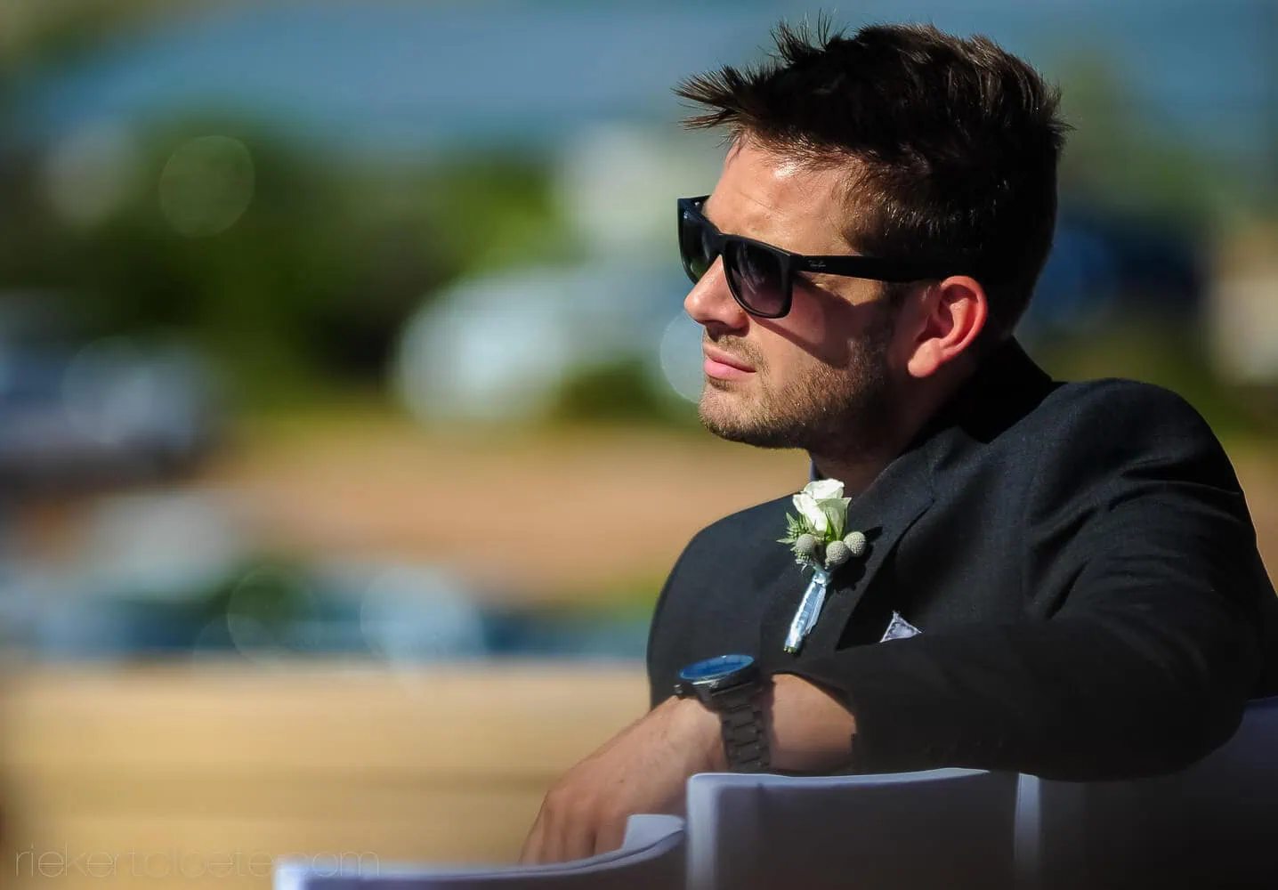 groom black suit sunglasses boutonniere coastal waiting