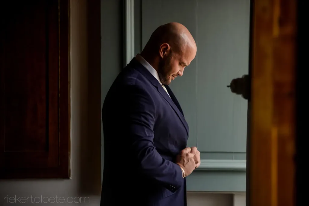 groom buttoning navy suit jacket window light