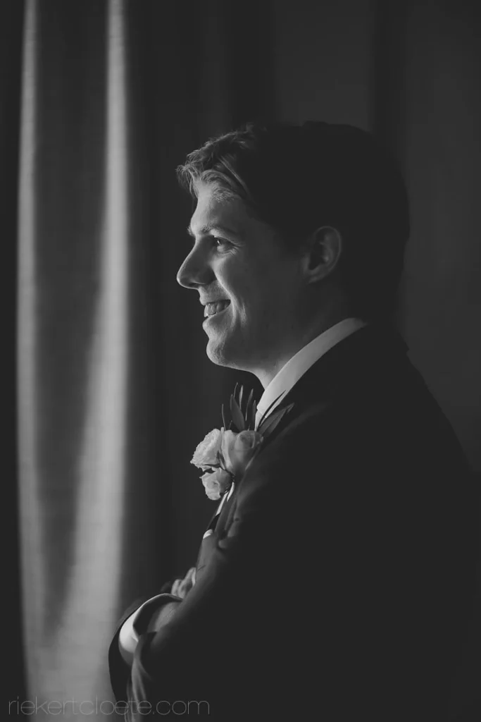 groom dark suit boutonniere arms crossed profile bw