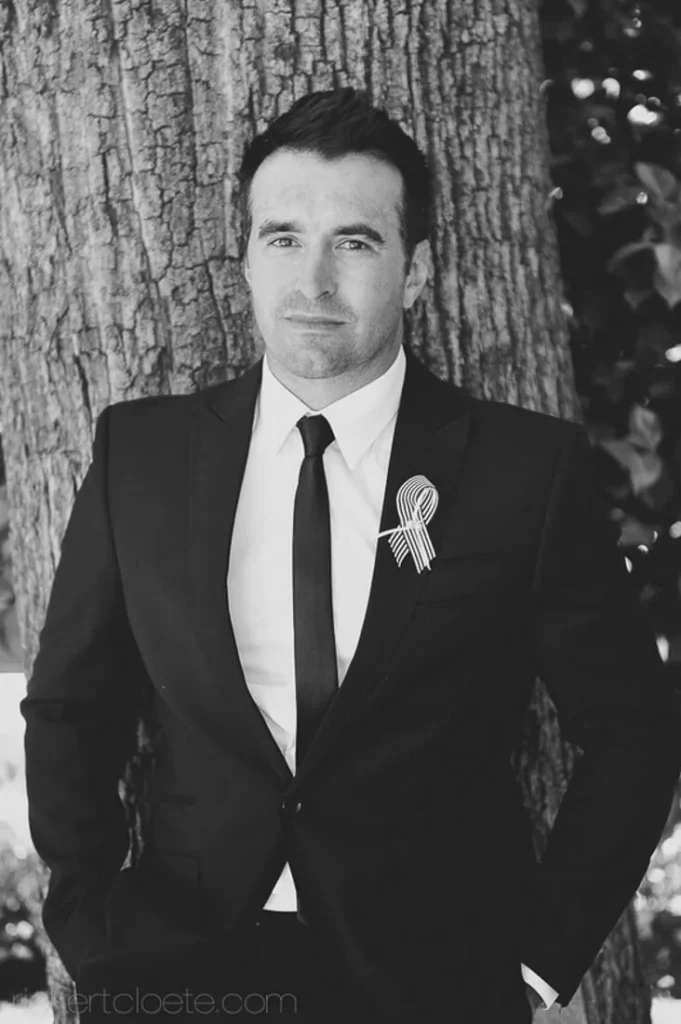 groom dark suit boutonniere tree outdoor portrait