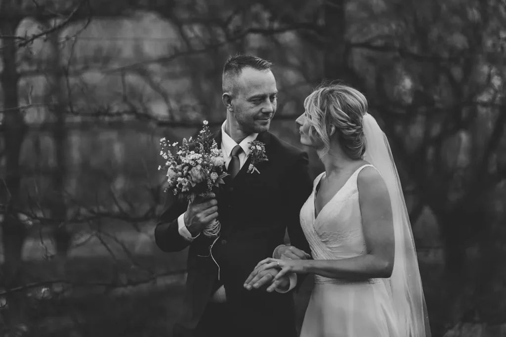 groom holds wildflower bouquet bride winter orchard