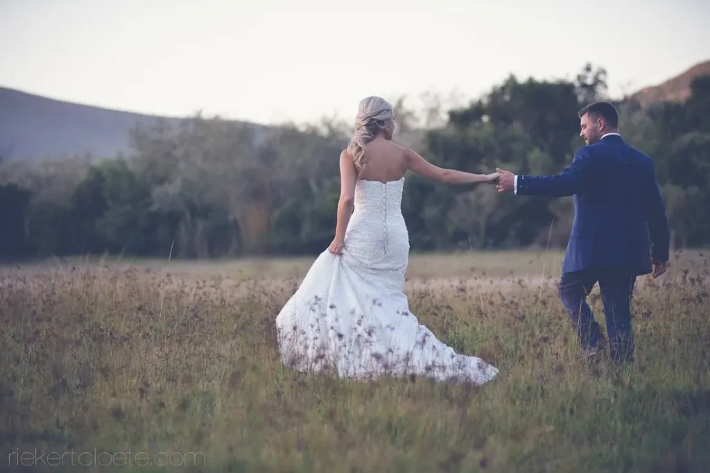 groom leading bride through golden meadow