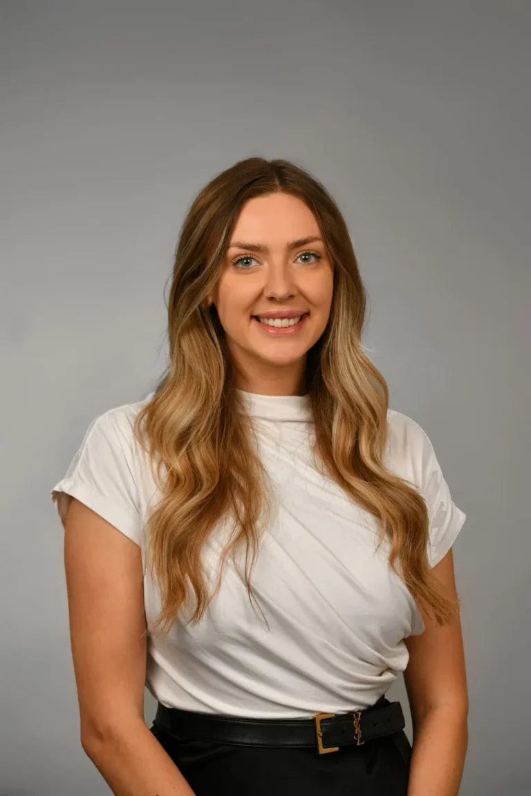 Woman smiling warmly, grey backdrop headshot
