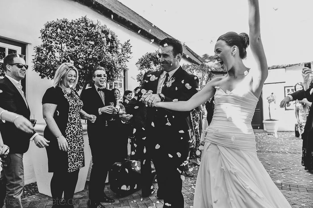 Couple laughing confetti exit cobblestone wine estate – Allée Bleue, Franschhoek