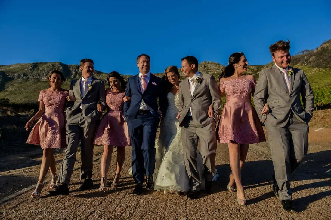 Bridal party laughing walking cape mountain backdrop – Cape Point Vineyards, Cape Town