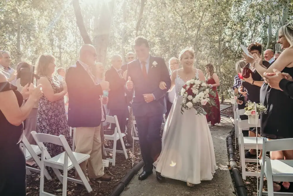 Bride forest aisle dappled light white garden chairs – D'Aria Winery, Durbanville