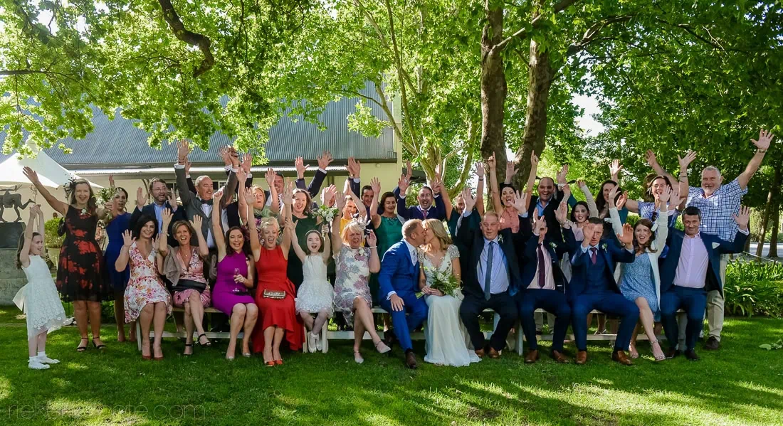 Wedding group seated on benches outside the Cape Dutch manor at Grande Provence estate, Franschhoek