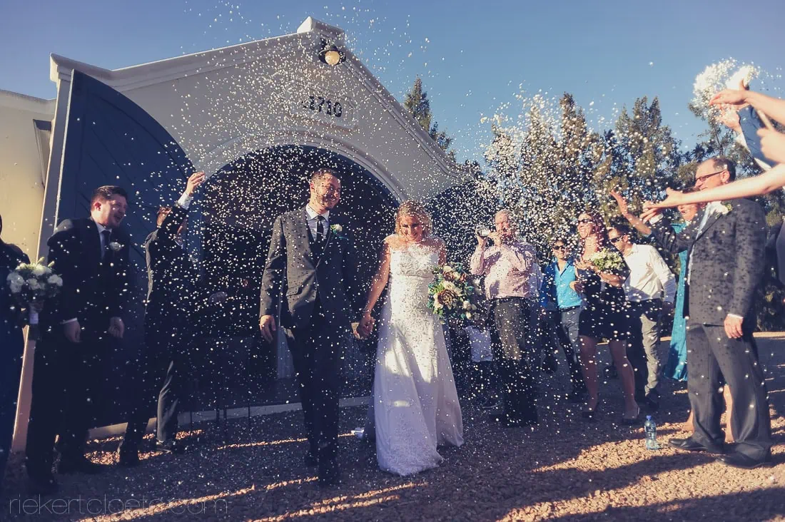Couple exiting arch gate heavy white confetti – Morgensvlei, Tulbagh
