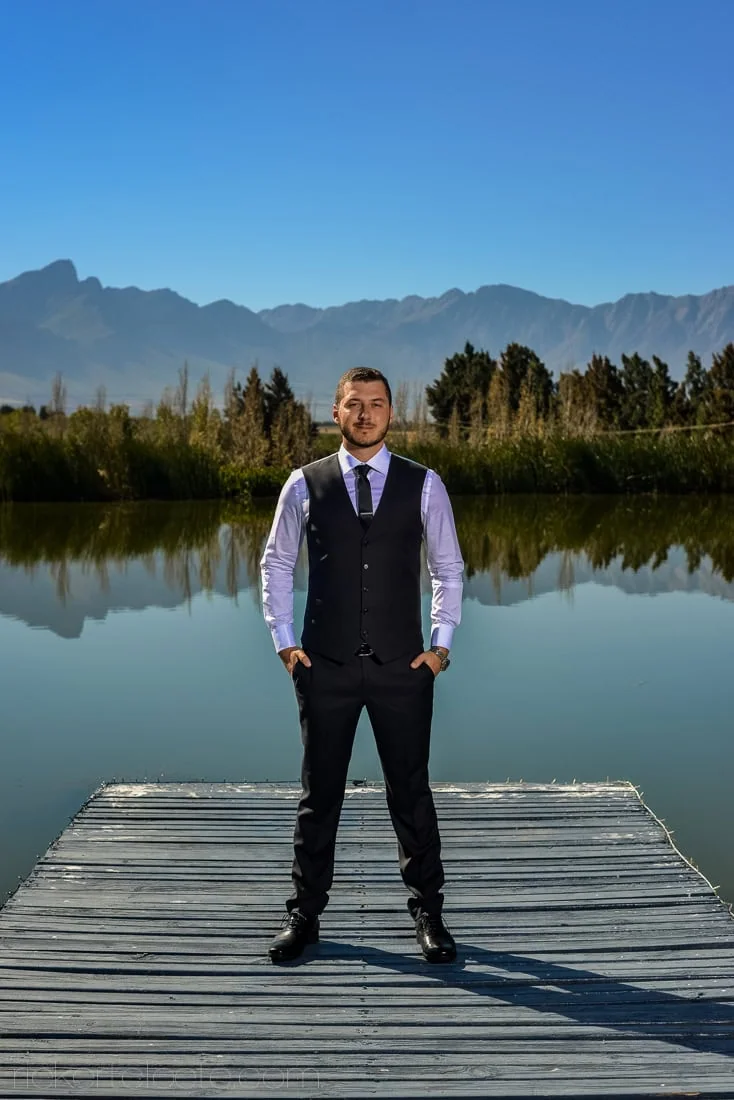 Groom dark vest jetty mountain water reflection – Morgensvlei, Tulbagh