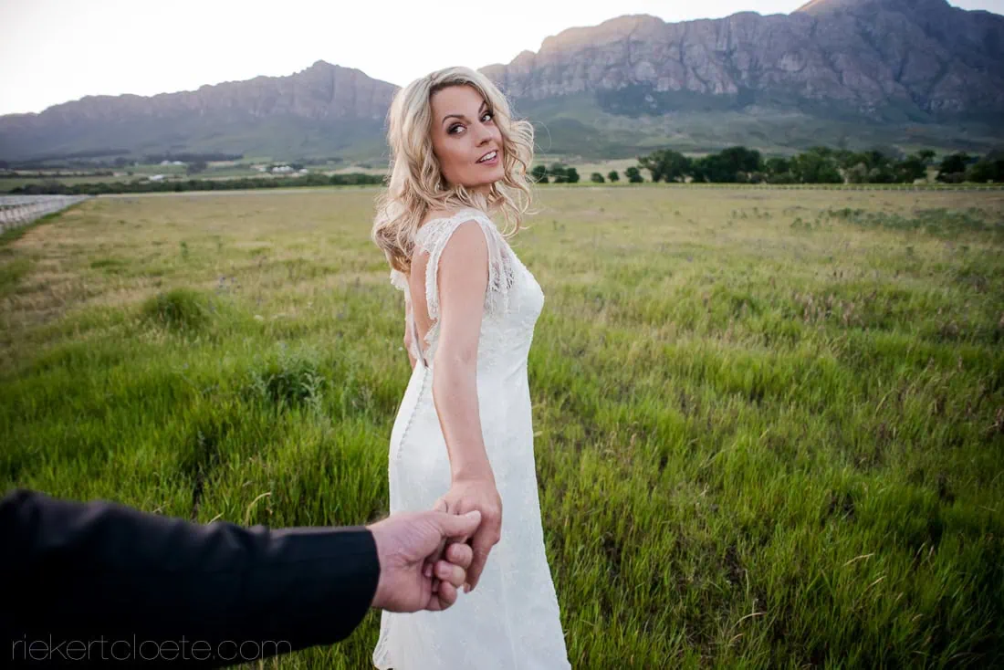 Bride leading groom green vineyard mountain views – Saronsberg Wine Cellar, Tulbagh