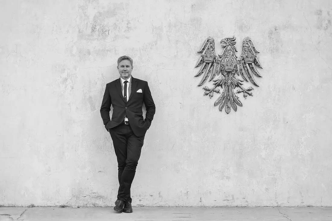 Groom full length black suit stone wall crest – Saronsberg Wine Cellar, Tulbagh