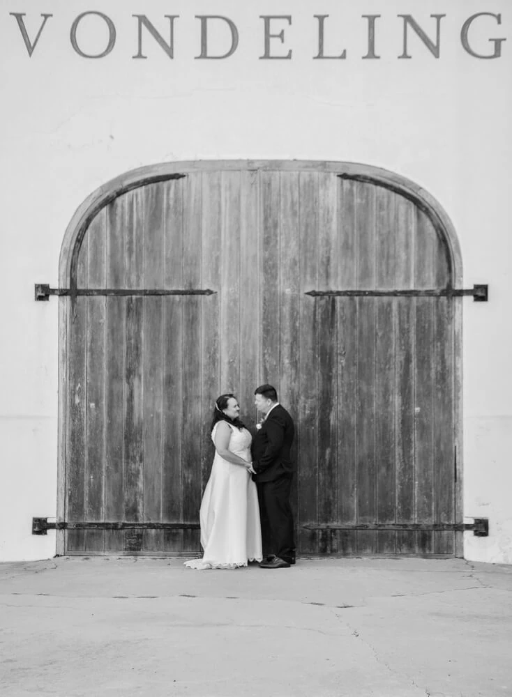 Vondeling couple kissing arched barn doors black white – Vondeling Wines, Paarl